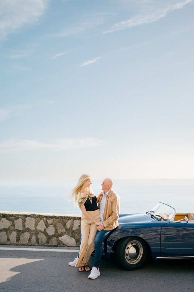 happy couple looking at each other sitting on a vintage car 