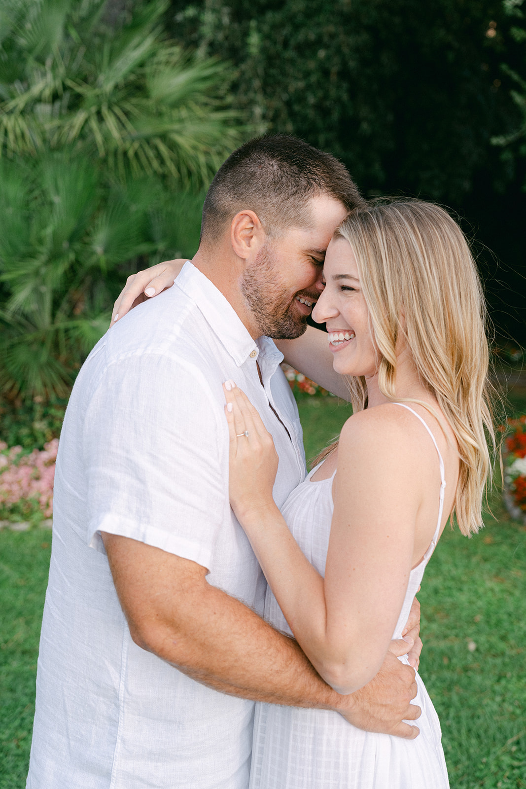 couple smiling hand hugging during engagement shoot wearing white linen