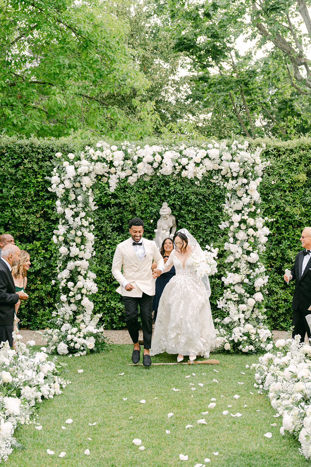 bride and groom jumping over a broom for traditional luck during wedding ceremony